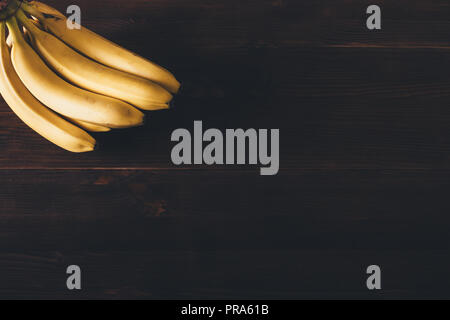 Bande de bananes biologiques sur table en bois brun foncé, vue du dessus. Un minimum de mise à plat arrangement avec fruits tropicaux mûrs jaune dans le coin avec vide Banque D'Images