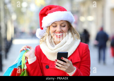 Vue avant portrait of a happy shopper shopping phone sur Noël dans la rue Banque D'Images