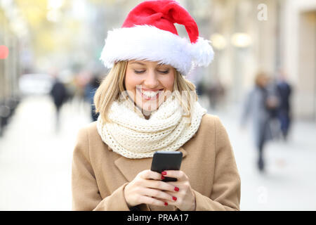 Happy woman wearing santa hat téléphone lecture texte sur Noël dans la rue Banque D'Images