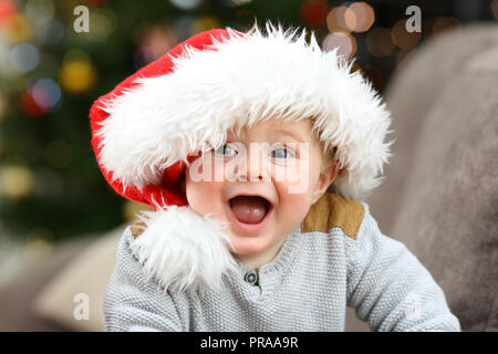 Heureux bébé portant un chapeau de Père Noël en vous regardant dans noël sur un canapé dans la salle de séjour à la maison Banque D'Images