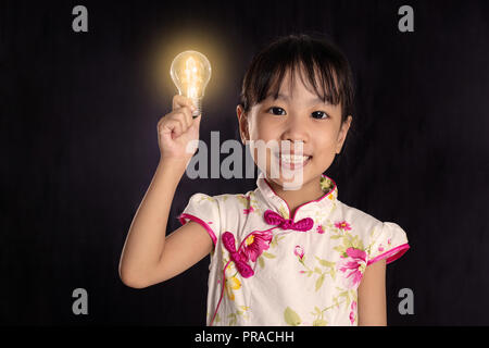 Chinois asiatique petite fille tenant une ampoule dans l'arrière-plan noir isolé Banque D'Images