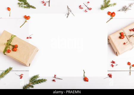 Carte de vœux de noël en blanc dans le cadre de branches de sapin, les fruits rouges, les coffrets cadeaux et les cônes over white background. maquette. Télévision. Vue de dessus Banque D'Images