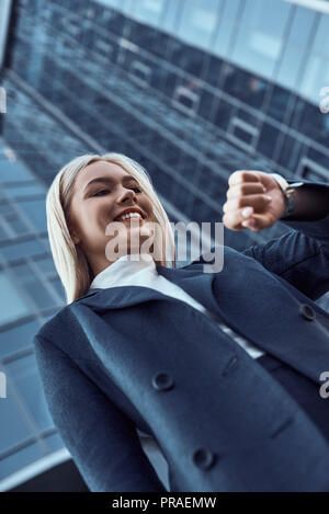 Femme regardant sa montre-bracelet en allant à l'office de consultation sur l'arrière-plan de la ville Banque D'Images