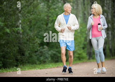 Happy senior couple jogging dans le parc entre les arbres verts dans la matinée Banque D'Images