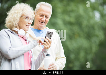 Des femmes plus âgées montrant son mari quelque chose en smartphone après entraînement en plein air Banque D'Images