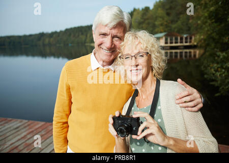 Heureux touristes mode dans l'habillement embrassant et smiling at camera while standing on pier et looking at camera, ils se reposant dans pays Banque D'Images
