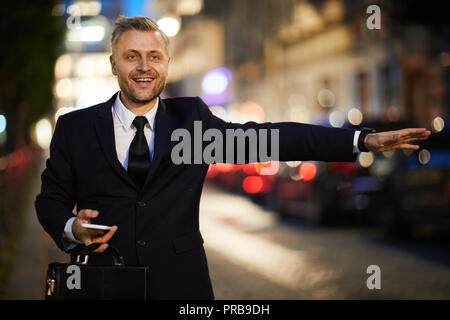 Homme heureux en soirée outstretching ses bras tout en regardant l'environnement urbain en taxi Banque D'Images