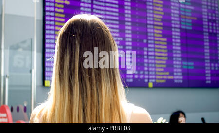 Vue arrière photo de jeune femme blonde à la recherche sur grand écran avec des temps de vol à l'aéroport Banque D'Images