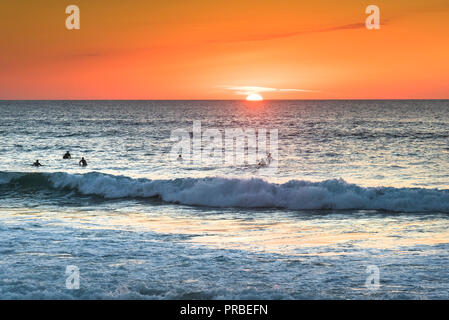 Les surfeurs en attente d'une vague silhouette par un coucher de soleil à la plage de Fistral à Newquay en Cornouailles. Banque D'Images