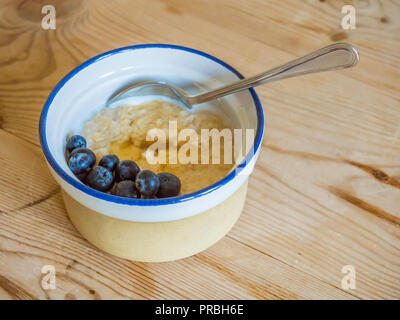 Plat de petit déjeuner porridge d'avoine dans un bol de lait en grès avec les bleuets et le miel sur une table en bois haut Banque D'Images