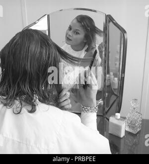 Le Maquillage dans les années 1950. Une jeune fille blonde est se coiffer devant le miroir. Avril 1954 Suède Banque D'Images