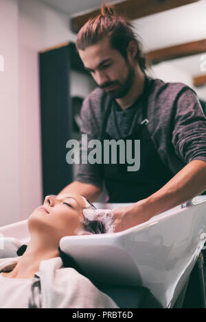 Young woman getting nouvelle coiffure coiffure professionnel au saloon. Coiffure est en massant son chef. Banque D'Images