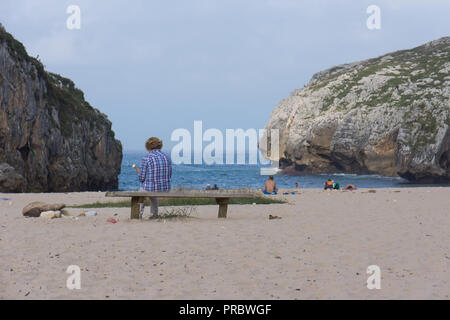 Vieille Femme assise sur un banc en bois sur une plage de sable fin avec un cornet de crème glacée à la mer, la plage de Cuevas del Mar, Barcelone, Espagne Banque D'Images