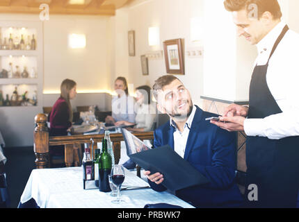 Dans l'ordre positif waiter taking restaurant, aider les jeunes hommes avec menu Banque D'Images