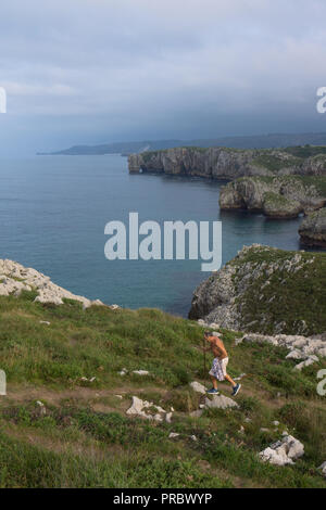 Homme marchant sur un chemin côtier le long de côte sauvage près de la plage de Cuevas del Mar, Llanes, Asturias, Espagne avec le nord de l'Espagne littoral en arrière-plan Banque D'Images