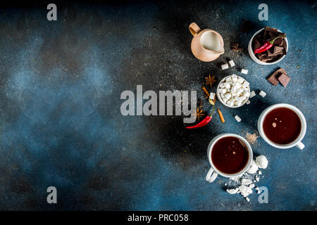 Tasses de chocolat chaud, morceaux de chocolat, sucre, guimauve, piment rouge et d'épices. Arrière-plan de béton bleu foncé top view space Banque D'Images