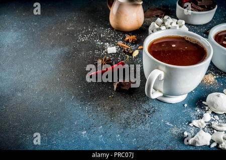 Tasses de chocolat chaud, morceaux de chocolat, sucre, guimauve, piment rouge et d'épices. Arrière-plan de béton bleu foncé top view space Banque D'Images