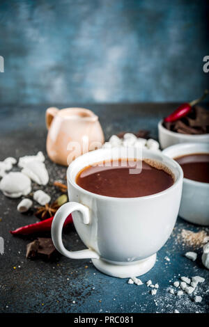 Tasses de chocolat chaud, morceaux de chocolat, sucre, guimauve, piment rouge et d'épices. Arrière-plan de béton bleu foncé top view space Banque D'Images