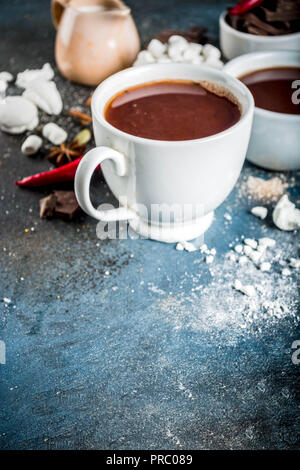 Tasses de chocolat chaud, morceaux de chocolat, sucre, guimauve, piment rouge et d'épices. Arrière-plan de béton bleu foncé top view space Banque D'Images