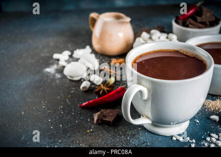 Tasses de chocolat chaud, morceaux de chocolat, sucre, guimauve, piment rouge et d'épices. Arrière-plan de béton bleu foncé top view space Banque D'Images