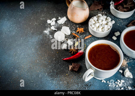 Tasses de chocolat chaud, morceaux de chocolat, sucre, guimauve, piment rouge et d'épices. Arrière-plan de béton bleu foncé top view space Banque D'Images