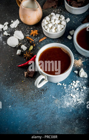 Tasses de chocolat chaud, morceaux de chocolat, sucre, guimauve, piment rouge et d'épices. Arrière-plan de béton bleu foncé top view space Banque D'Images