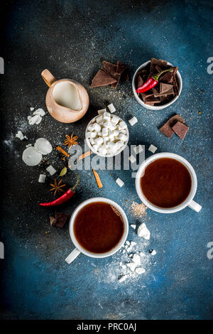 Tasses de chocolat chaud, morceaux de chocolat, sucre, guimauve, piment rouge et d'épices. Arrière-plan de béton bleu foncé top view space Banque D'Images