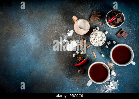 Tasses de chocolat chaud, morceaux de chocolat, sucre, guimauve, piment rouge et d'épices. Arrière-plan de béton bleu foncé top view space Banque D'Images