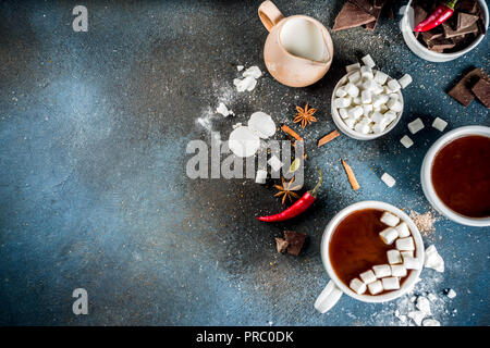 Tasses de chocolat chaud, morceaux de chocolat, sucre, guimauve, piment rouge et d'épices. Arrière-plan de béton bleu foncé top view space Banque D'Images