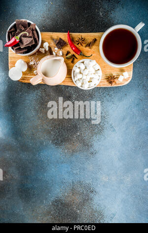 Tasses de chocolat chaud, morceaux de chocolat, sucre, guimauve, piment rouge et d'épices. Arrière-plan de béton bleu foncé top view space Banque D'Images