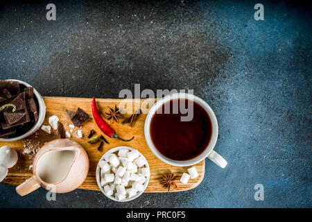 Tasses de chocolat chaud, morceaux de chocolat, sucre, guimauve, piment rouge et d'épices. Arrière-plan de béton bleu foncé top view space Banque D'Images