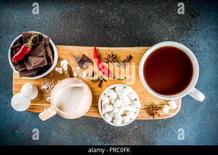 Tasses de chocolat chaud, morceaux de chocolat, sucre, guimauve, piment rouge et d'épices. Arrière-plan de béton bleu foncé top view space Banque D'Images