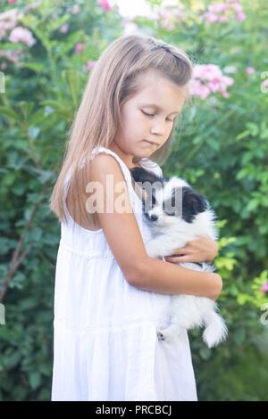 Petite fille tenant un chiot dans ses bras dans le jardin Banque D'Images