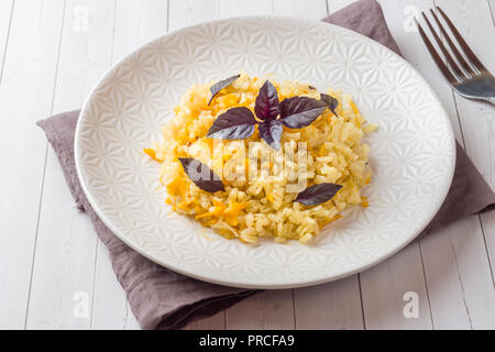 Pilaf traditionnel, riz aux légumes et basilic frais dans une assiette sur une table en bois clair Banque D'Images