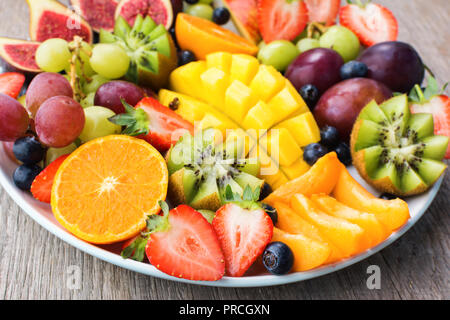 Un assortiment de fruits et de baies, fraises, bleuets plateau orange Mangue, Pommes, raisins, kiwis sur le fond en bois gris Banque D'Images