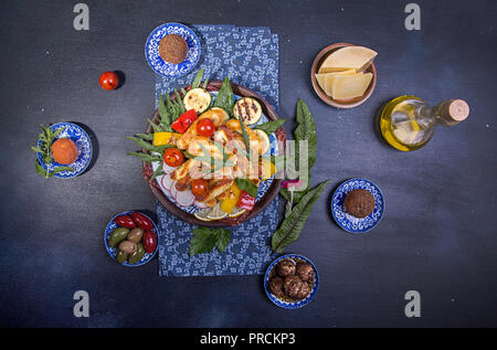 Ensemble prédéfini de fromage et des collations. Halloumi grillé, belper knolle, olives, sauce tzatziki sur bleu profond sur fond noir. Les frais généraux. Banque D'Images