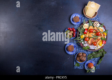 Ensemble prédéfini de fromage et des collations. Halloumi grillé, belper knolle, olives, sauce tzatziki sur bleu profond sur fond noir. Les frais généraux. Copier l'espace. Banque D'Images