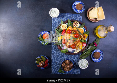 Ensemble prédéfini de fromage et des collations. Halloumi grillé, belper knolle, olives, sauce tzatziki sur bleu profond sur fond noir. Les frais généraux. Copier l'espace. Banque D'Images