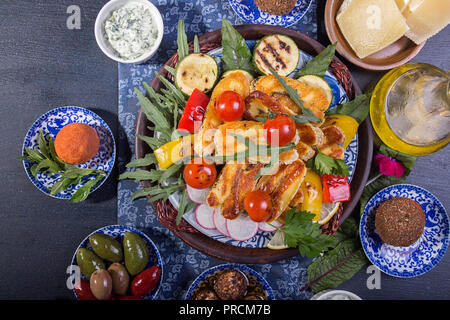 Ensemble prédéfini de fromage et des collations. Halloumi grillé, belper knolle, olives, sauce tzatziki sur bleu profond sur fond noir. Les frais généraux. Banque D'Images