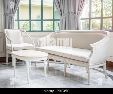 Vintage luxury white canapé, fauteuil et table près de la fenêtre en verre et des rideaux sur en marbre dans la maison contemporaine avec l'arbre et à l'extérieur du bâtiment. Banque D'Images
