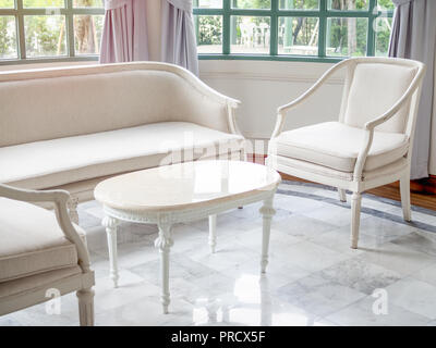 Vintage luxury white canapé, fauteuil et table près de la fenêtre en verre et des rideaux sur en marbre dans la maison contemporaine avec l'arbre et à l'extérieur du bâtiment. Banque D'Images