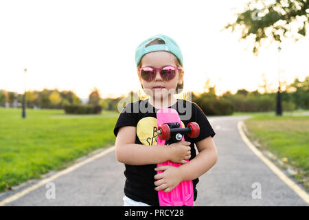 Petite fille mode enfant avec skateboard portant une chemise hippie et lunettes. Banque D'Images