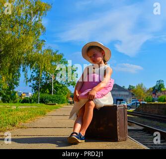 Cute girl holding peluche sur une gare, attendant le train avec vintage suitcase. Les voyages, vacances et enfance concept. 09/12/2012 10 voyages Banque D'Images