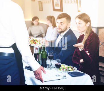 Jeune couple insatisfaits se disent insatisfaits avec la nourriture pour parler en excuses waiter Banque D'Images