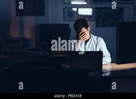 Épuisé Asian businessman travaillant tard dans la nuit dans un bureau Banque D'Images