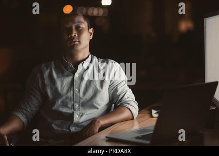 Asian businessman assis à son bureau dans un bureau sombre Banque D'Images