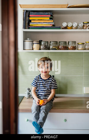 Petit garçon dans la cuisine holding orange Banque D'Images