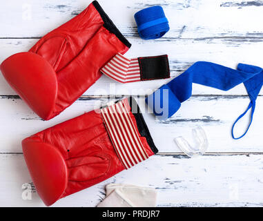 Paire de gants de boxe en cuir rouge, bleu, pansement textile Protection silicone pour les dents sur un fond en bois blanc, vue du dessus Banque D'Images