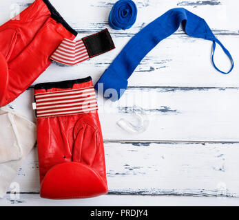 Paire de gants de boxe en cuir bleu, rouge bandage et silicone bouche cap sur un fond en bois blanc, vue du dessus Banque D'Images