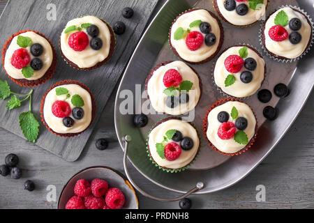 Muffins au chocolat ou des petits gâteaux avec de la crème fouettée et de petits fruits, de mise à plat sur fond de bois rustique gris Banque D'Images